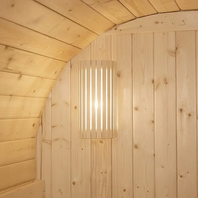 Home Deluxe Fasssauna CUBE L - Elektroofen, Holz - Hölzerne Lattenwandleuchte spendet sanftes Licht, an heller Holzverkleidung montiert.
