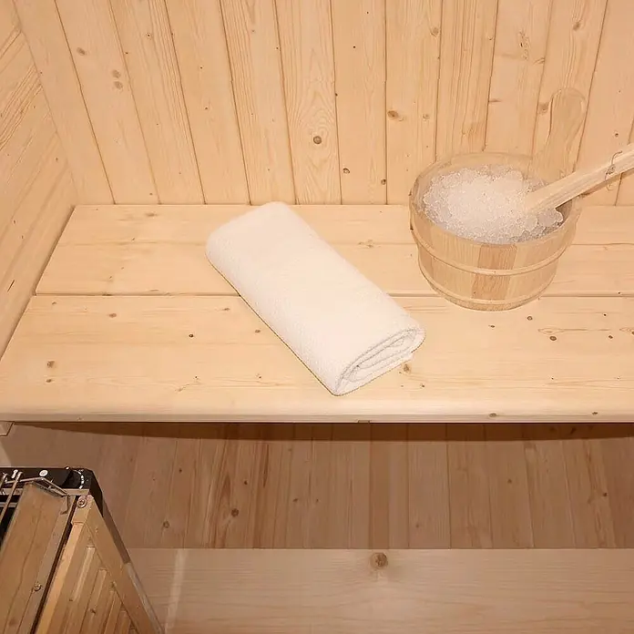 Home Deluxe Fasssauna CUBE S - Elektroofen, Holz - Hölzerner Sauna-Innenraum mit gefaltetem weißen Handtuch und Holzeiskübel auf einer Bank.