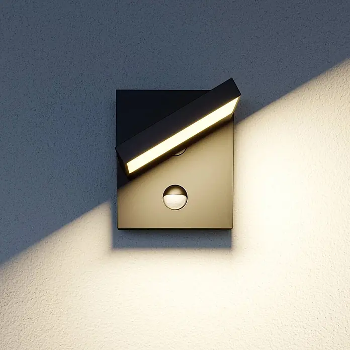 Lucande Außenwandleuchte Silvan - 17,5 x 14 x 16,1 cm, schwarz, IP54 - Dunkle quadratische Wandleuchte mit verstellbarer LED-Leiste, warmem Licht und Bewegungssensor an einer strukturierten Wand.