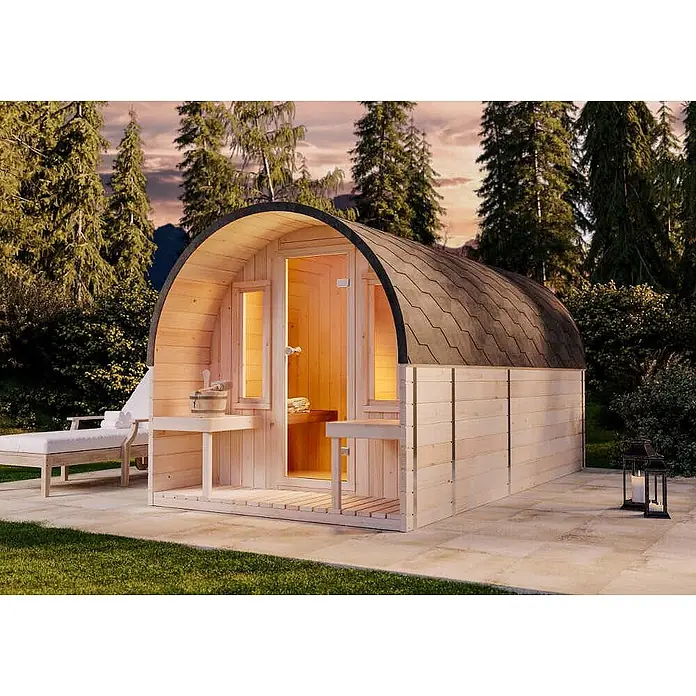 FinnTherm Fasssauna ScandiPod Deluxe - Holz, L x B x H: 406 x 21 x 210 cm - Hellholz-Fasssauna mit dunklem Dach auf einer Außenterrasse, ausgestattet mit Eimer und Liegestuhl.