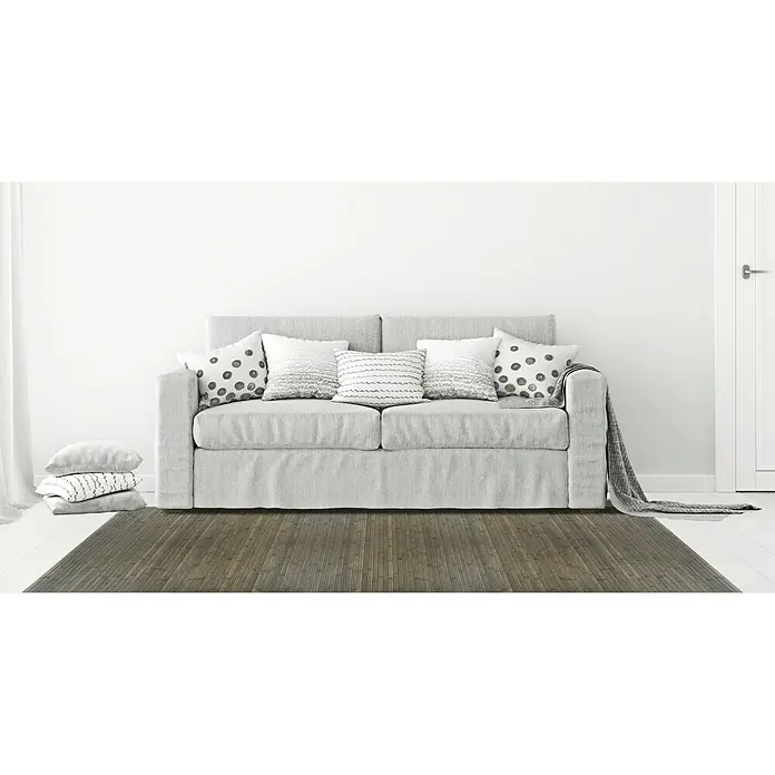 Alfombra de bambú Cool - Gris, 150 x 80 cm - Un sofá gris con cojines y una manta frente a una pared blanca, con una alfombra de patrón de tablones de madera.