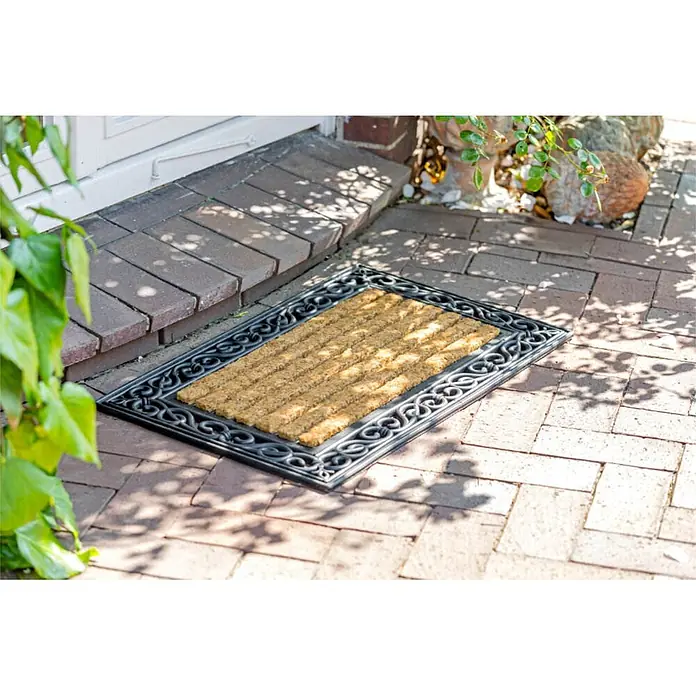 Kai Wiechmann Fußmatte - 46 x 76 cm - Braune Kokos-Fußmatte mit schwarzem, verziertem Gummirahmen auf einer Ziegelterrasse vor einer Tür.