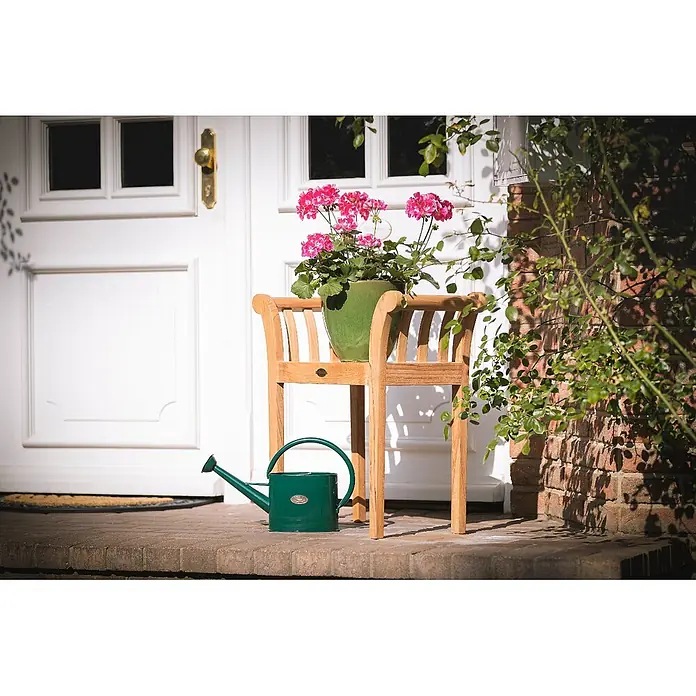 Kai Wiechmann Gartenhocker - Teakholz, braun - Heller Pflanzenständer aus Holz auf einer Veranda, mit grünem Topf voller rosa Blüten und grüner Gießkanne daneben.