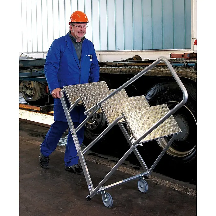 Munk Arbeitsplattform Arbeitspodest starr mit Handlauf 4 Stufen - Anzahl Tritte: 4 Stk., Arbeitshöhe: 2.800 m, Aluminium - Mann schiebt eine tragbare Aluminium-Arbeitsplattform mit Riffelblech-Stufen und Rollen, zum Zugang für LKWs.