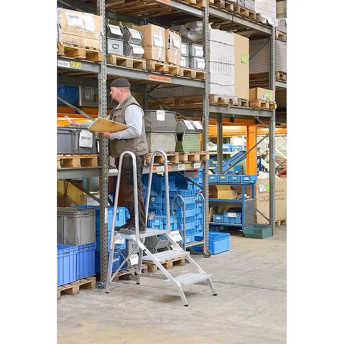 Hymer Arbeitsplattform Treppentritt Montagetritt 2 Stufen - Anzahl Tritte: 2 Stk., Arbeitshöhe: 2.480 m, Aluminium - Silberne Aluminium-Arbeitsplattform mit Stufen, von einem Mann im Lager für hohe Regale genutzt.