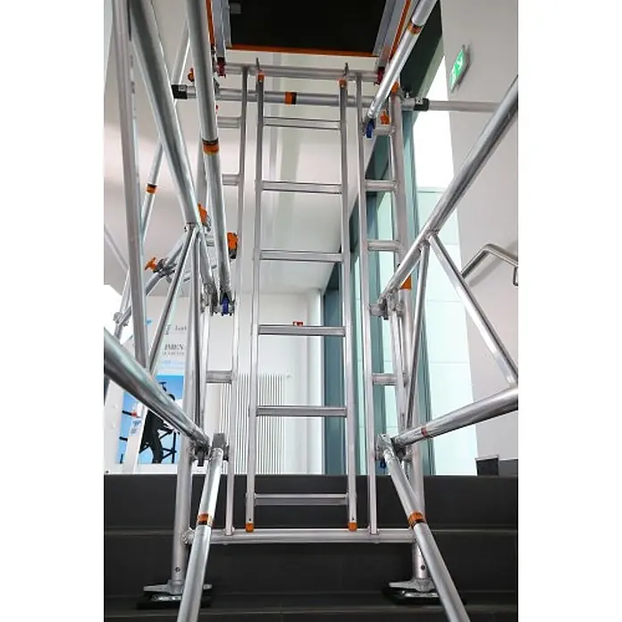 Layher Rollgerüst Treppen-Kit für Fahrgerüst Uni Standard P2 mit 2 Durchgängen 7,73m AH - Arbeitshöhe: 7.730 m - Silbernes Aluminium-Zugangsgerüst auf einer Innentreppe aufgebaut.