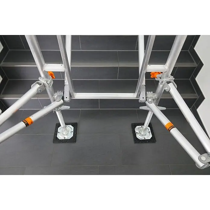 Layher Rollgerüst Treppen-Kit für Fahrgerüst Uni Standard P2 mit 2 Durchgängen 7,73m AH - Arbeitshöhe: 7.730 m - Aluminium-Gerüstunterbau mit verstellbaren Beinen und Schutzplatten, auf dunklen gefliesten Treppen aufgestellt.