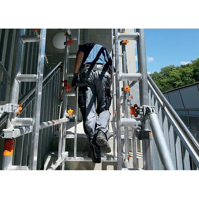 Layher Rollgerüst Treppen-Kit für Fahrgerüst SoloTower mit 2 Durchgängen 4,65m AH - Arbeitshöhe: 4.650 m - Arbeiter besteigt eine silbergraue Gerüsttreppe mit orangen Sterngriffen, die Robustheit und Zugänglichkeit unterstreicht.
