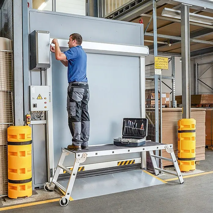 Zarges Arbeitsplattform Arbeitsplattform klappbar Workmaster Plus P Holz Plattformbelag - Anzahl Tritte: 3 Stk., Arbeitshöhe: 2.700 m, Aluminium - Mann auf mobiler Aluminium-Arbeitsplattform mit dunkler Antirutschfläche, arbeitet an einer Industrietafel. Werkzeugkoffer darauf.