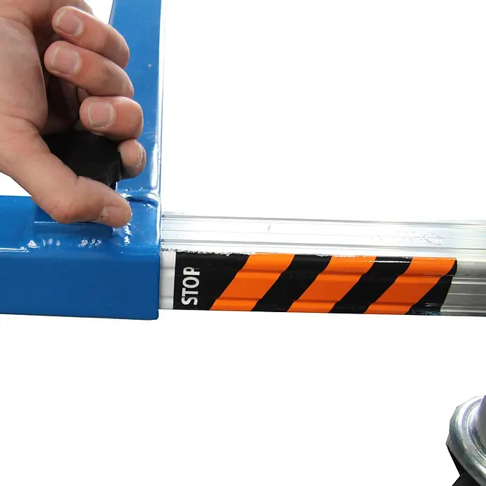ASC Arbeitsplattform XS-Lift Hebebühne mit 3,8m Arbeitshöhe - Arbeitshöhe: 3.800 m, Belastbarkeit: 120 kg, Aluminium - Hand verstellt einen schwarzen Drehknopf an einem blauen Metallrahmen, neben einer silbernen Stange mit orange-schwarzem „STOP“-Warnschild.
