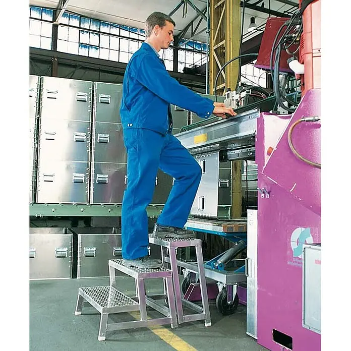Zarges Arbeitsplattform Aluminium-Arbeitspodest AMA P Modul A - Arbeitshöhe: 2.200 m, Aluminium - Industrieller 3-Stufen-Hocker aus Metall mit rutschfesten Trittflächen, von Arbeiter an Maschine genutzt.