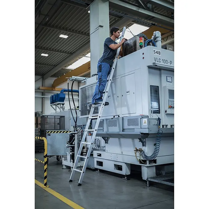 Munk Anlegeleiter Anlegeleiter 8 Sprossen - Anzahl Tritte: 8 Stk., Arbeitshöhe: 3.600 m, Aluminium - Silberne Aluminium-Stehleiter in einer Industrieumgebung, ein Mann nutzt sie zur Arbeit an einer großen Maschine.
