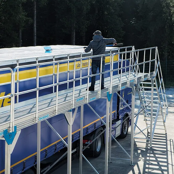 Zarges Plattformgerüst Enteisungsbühne Basismodul mit Treppenzugang 3m Höhe 6m Länge - Arbeitshöhe: 4.800 m - Mobile Aluminium-Arbeitsplattform mit Treppe, die sicheren Zugang zum Dach eines blauen LKW-Anhängers bietet, auf dem eine Person arbeitet.