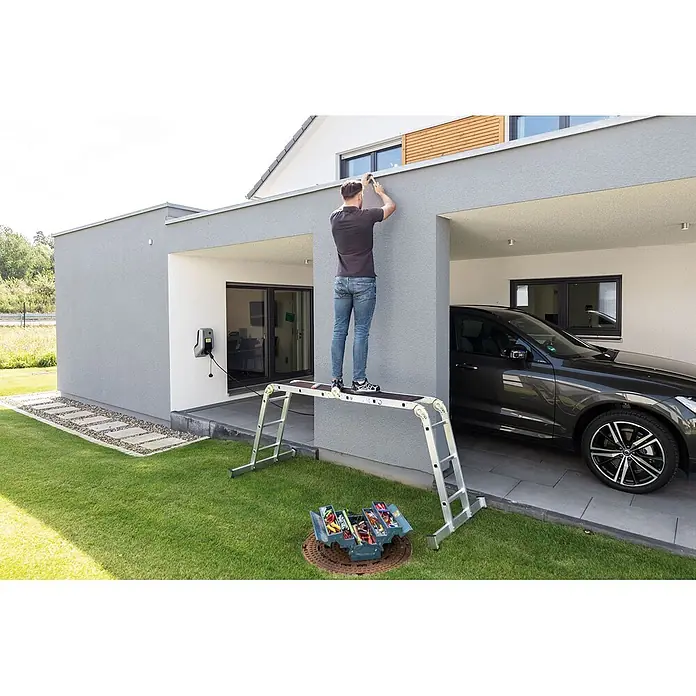 Munk Mehrzweckleiter Vielzweckleiter mit Nivello® Traverse und Holzbelag 2x2 + 2x3 Sprossen - Arbeitshöhe: 4.000 m, Aluminium - Silberne Multifunktionsleiter/Arbeitsplattform unterstützt Person bei Fassadenarbeiten. Werkzeugkasten am Boden.