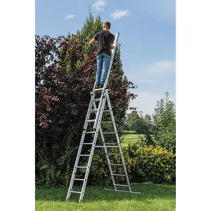 Munk Mehrzweckleiter Mehrzweckleiter mit Nivello® Traverse 3x7 Sprossen - Anzahl Tritte: 7 Stk., Arbeitshöhe: 6.100 m, Aluminium - Mann beschneidet hohen Baum mit einer silbernen Aluminium-Mehrzweckleiter im Garten.