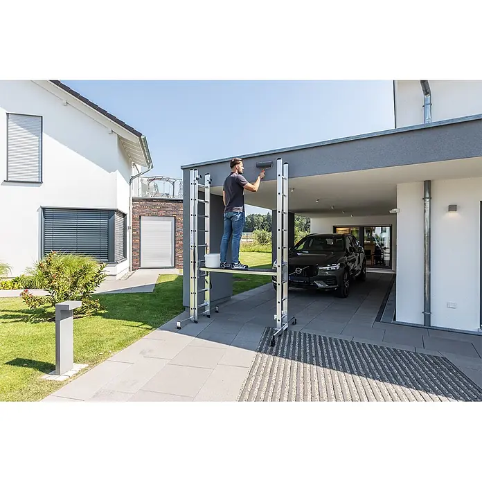 Munk Mehrzweckleiter Mehrzweckleiter mit Nivello® Traverse 3x9 Sprossen - Anzahl Tritte: 9 Stk., Arbeitshöhe: 7.800 m, Aluminium - Aluminium Rollgerüst wird von einem Mann zum Streichen eines Carports verwendet.