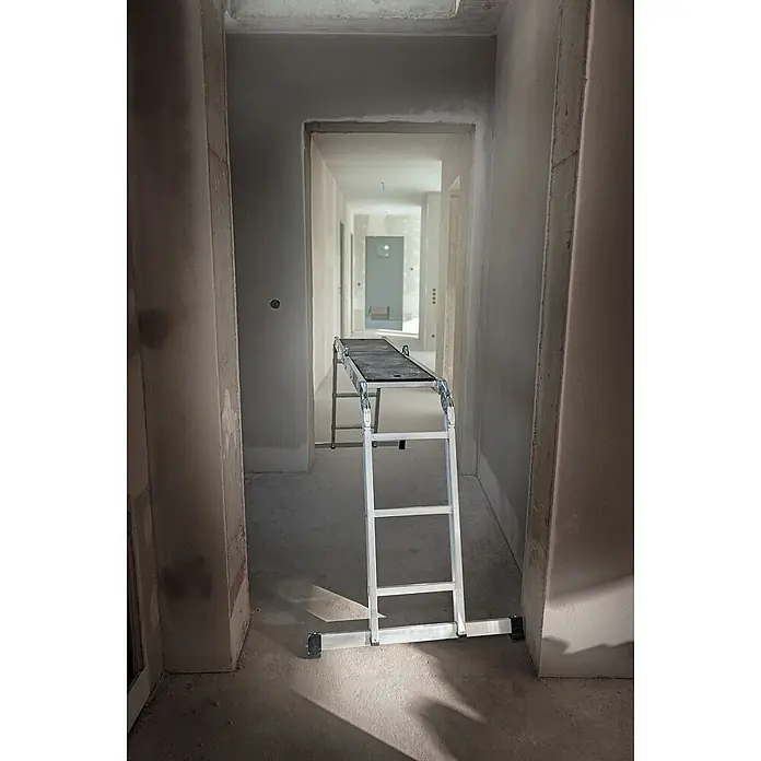Werner Mehrzweckleiter Vielzweckleiter 4-teilig mit Plattform - Anzahl Tritte: 3 Stk., Arbeitshöhe: 4.540 m, Aluminium - Silberne Aluminium-Arbeitsplattform mit schwarzer Oberfläche, in einem unfertigen Flur für Bauarbeiten aufgestellt.