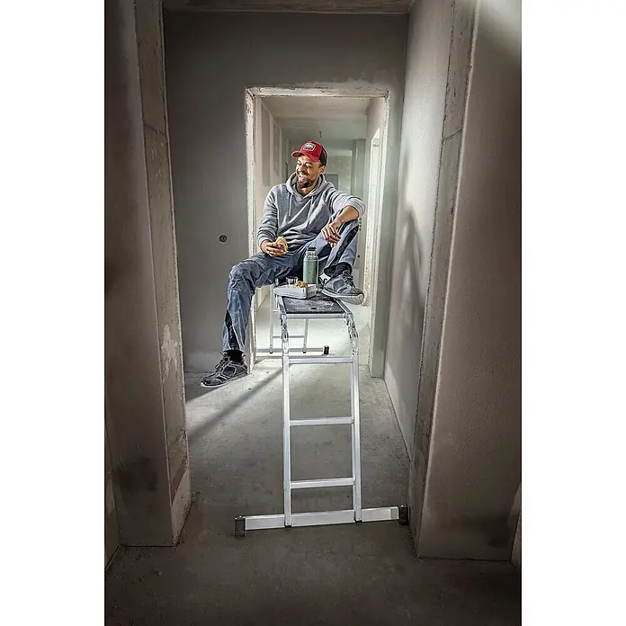 Werner Mehrzweckleiter Vielzweckleiter 4-teilig mit Plattform - Anzahl Tritte: 3 Stk., Arbeitshöhe: 4.540 m, Aluminium - Silberne Aluminium-Arbeitsplattform, die von einem Bauarbeiter in einem Flur als Pause genutzt wird.