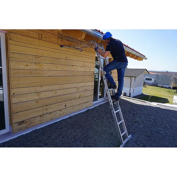 Mauderer Mehrzweckleiter Bavaria Sechsgelenkleiter als Behelfsgerüst mit Rastgelenk und gebogener T - Anzahl Tritte: 3 Stk., Arbeitshöhe: 4.400 m, Belastbarkeit: 150 kg - Ein Mann mit blauem Helm benutzt eine silberne Mehrzweckleiter, um an der Holzfassade eines Gebäudes nahe der Dachrinne zu arbeiten.