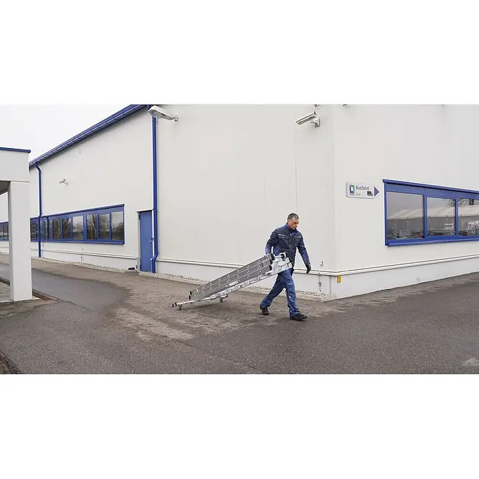 Munk Mehrzweckleiter Stufen- Mehrzweckleiter mit Wandlaufrollen, clipstep R13 und Nivello® Trav - Anzahl Tritte: 8 Stk., Arbeitshöhe: 6.900 m, Aluminium - Mann trägt eine silberne Mehrzweck-Klappleiter mit Rollen über einen gepflasterten Bereich.
