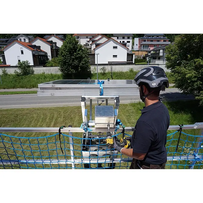 Mauderer Mehrzweckleiter Bavaria Leiterlift bis max. Förderhöhe 8,60m 2x16 Sprossen - Anzahl Tritte: 16 Stk., Belastbarkeit: 100 kg, Aluminium - Mann bedient gelbes Elektrowerkzeug an einer silbernen Solarmodul-Hebevorrichtung mit Solarmodulen, in Wohnumgebung.