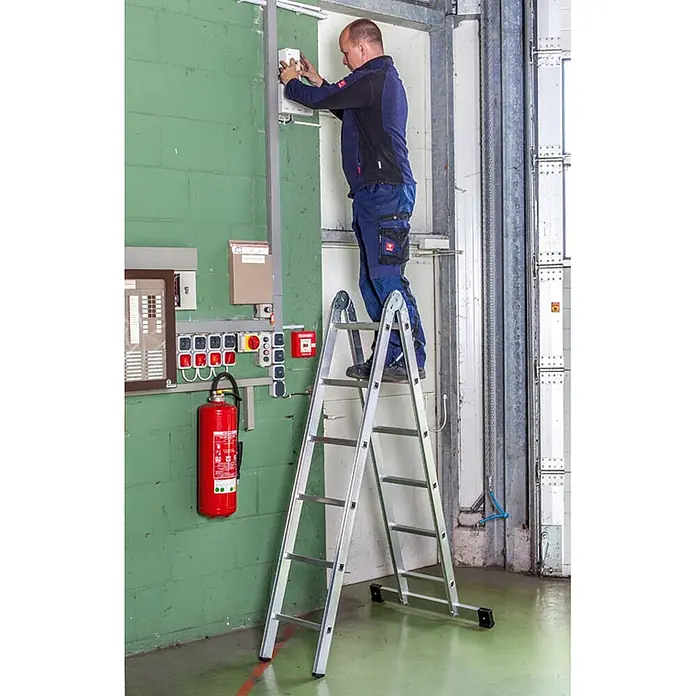 Euroline Mehrzweckleiter Premium 317 Klappleiter 2x6 Sprossen - Anzahl Tritte: 6 Stk., Arbeitshöhe: 4.350 m, Aluminium - Mann arbeitet an einem Schaltkasten, während er auf einer silbernen Aluminium-Klappleiter steht.