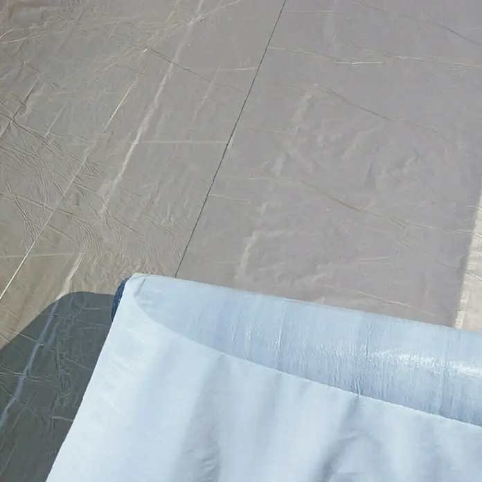 Karibu Premium Dachbahn - Silbergrau, Selbstklebend - Nahaufnahme einer Rolle hellblauer, glänzender wasserdichter Plane auf einer grauen Oberfläche, ideal für Bau- oder Abdeckarbeiten.