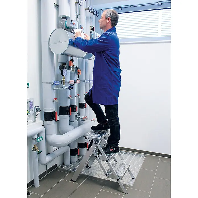 Munk Klapptritt kompakt Tritt ML 2 Stufen - Arbeitshöhe: 2.450 m, Aluminium - Aluminium-Klapptritt, von einem Mann für Wartungsarbeiten an hohen Rohren verwendet.