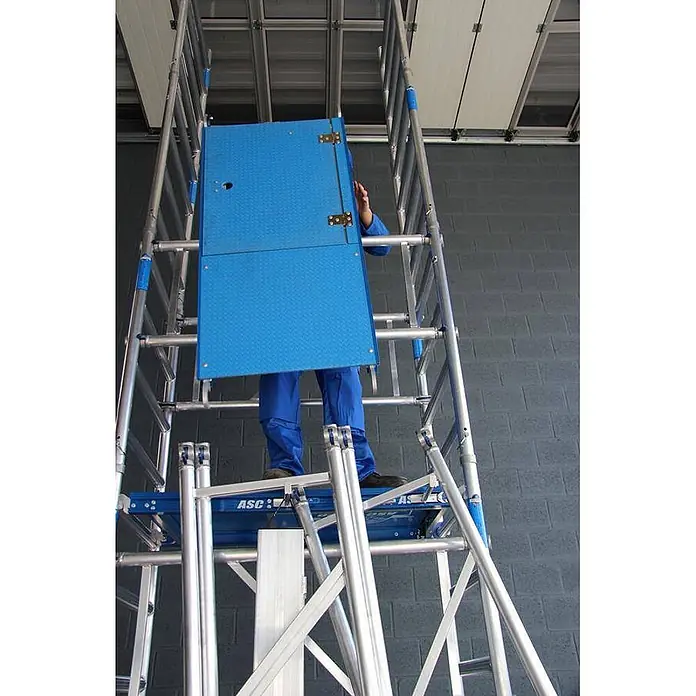 ASC Rollgerüst Rollgerüst XS-Tower (DIN EN 1004:2004) - Arbeitshöhe: 6.200 m - Arbeiter in Blau auf einem Aluminium-Rollgerüst, nutzt blaue Durchstiegplattform mit Tür für sicheren Zugang zur nächsten Ebene.