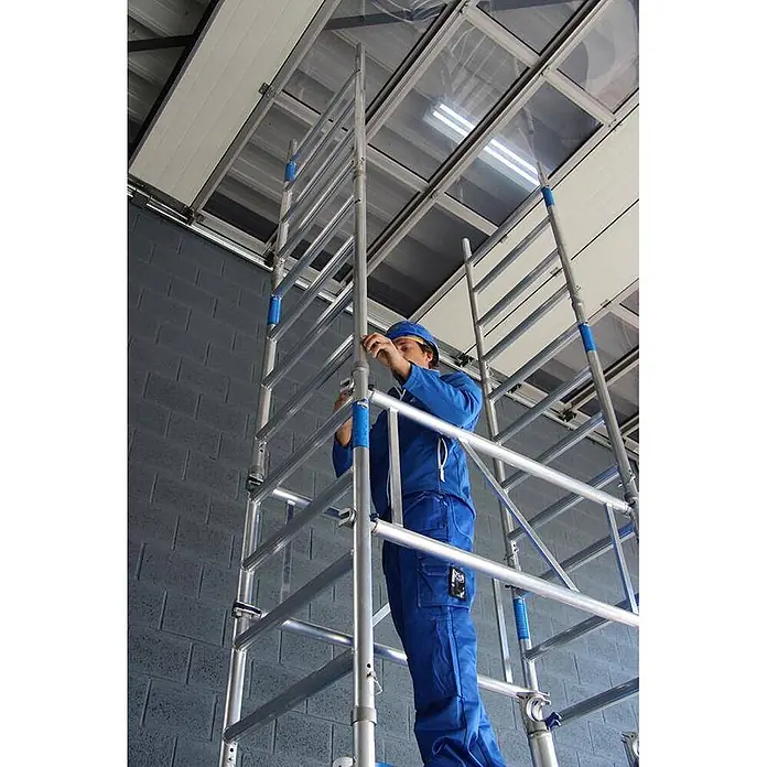 ASC Rollgerüst Rollgerüst XS-Tower (DIN EN 1004:2004) - Arbeitshöhe: 6.200 m - Arbeiter in Blau montiert ein silbernes Aluminiumgerüst mit blauen Akzenten in Innenräumen.