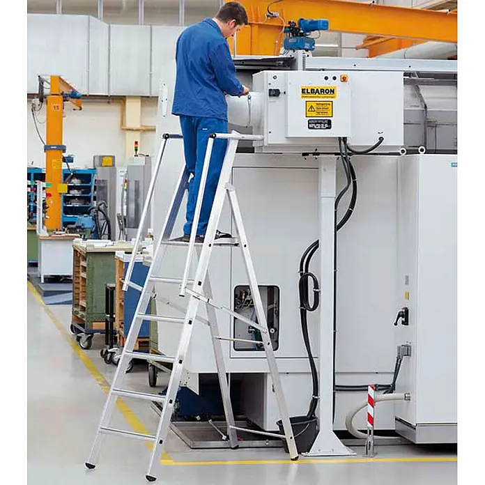 Zarges Stehleiter Stufenleiter ZAP Safemaster S mit großer Plattform 9 Stufen - Anzahl Tritte: 9 Stk., Arbeitshöhe: 4.340 m, Aluminium - Silberne Aluminium-Klappleiter, auf der ein Arbeiter eine Maschine in einer Fabrik erreicht.