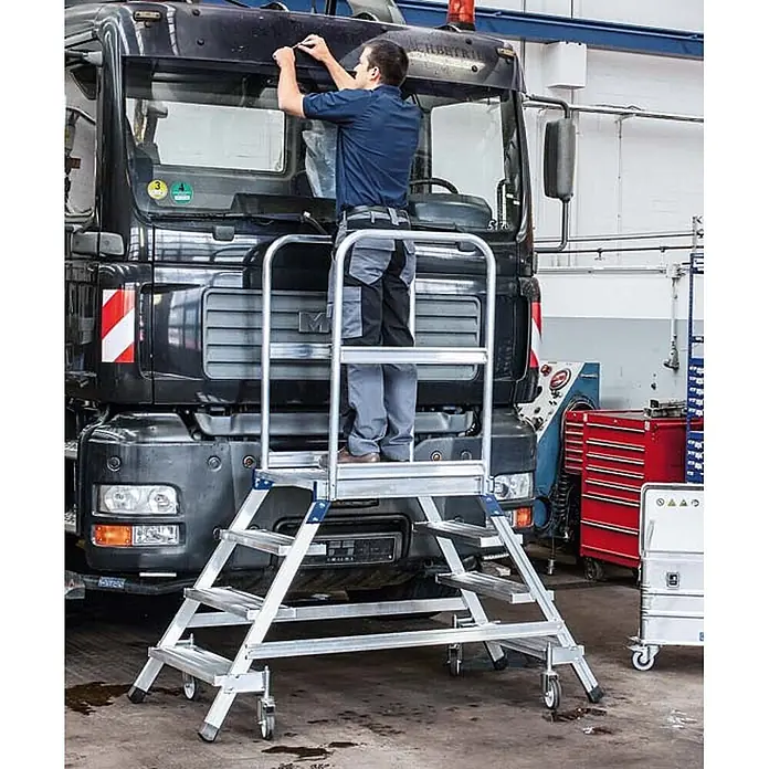 Zarges Podestleiter Podestleiter fahrbar mit 2x5 Leichtmetall-Stufen - Anzahl Tritte: 5 Stk., Aluminium - Mobile Arbeitsplattform aus silbernem Aluminium mit Stufen und Geländern, von einem Arbeiter zur Wartung an einer LKW-Windschutzscheibe genutzt.