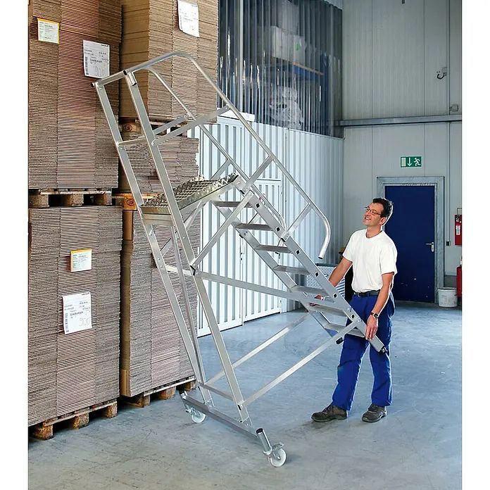 Munk Treppenpodest Plattformleiter fahrbar 9 Stufen - Anzahl Tritte: 9 Stk., Arbeitshöhe: 4.100 m, Aluminium - Mobile Aluminium-Arbeitsplattform mit Rollen, von einem Mann zum Erreichen hoher Kartonstapel im Lager genutzt.