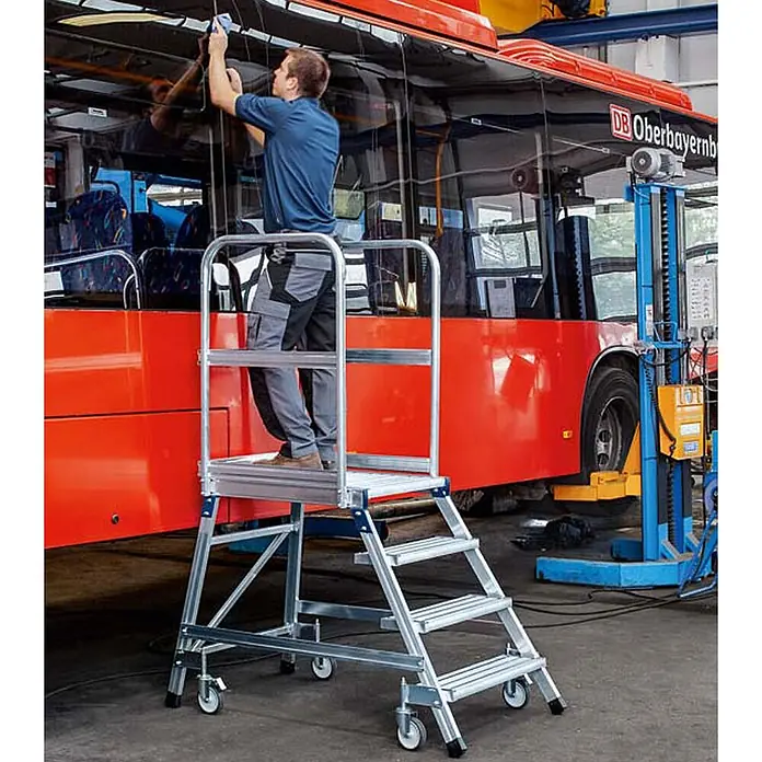 Zarges Podestleiter Podestleiter fahrbar mit 5 Stahl-Giterrost-Stufen - Anzahl Tritte: 5 Stk., Aluminium - Mobile Arbeitsplattform aus silbernem Aluminium mit Stufen und Rollen, ein Mann nutzt sie für Arbeiten an einem Bus.