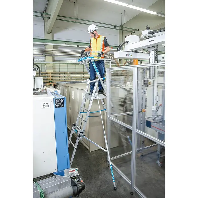 Zarges Teleskopleiter Teleskop Plattformleiter ZAP MASTERFLEX S 7-9 Sprossen - Anzahl Tritte: 7 Stk., Arbeitshöhe: 4.300 m, Belastbarkeit: 150 kg, Aluminium - Multifunktionale silberne Aluminium-Arbeitsplattform mit blauen Akzenten, von einem Arbeiter in einer Industrieumgebung genutzt.