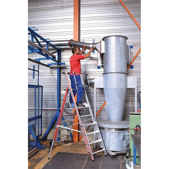 Hymer Teleskopleiter Plattformleiter Protect+ mit Teleskopausleger und Sicherheitstüren 5-8 Spr - Arbeitshöhe: 3.770 m, Aluminium - Verstellbare Aluminium-Stehleiter mit roten Akzenten, die einen Arbeiter bei Wartungsarbeiten an Industriemaschinen unterstützt.