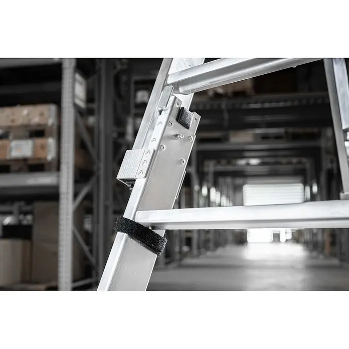 Munk Stehleiter Stufen Stehleiter beidseitig begehbar steckbar 2x4 Stufen - Anzahl Tritte: 4 Stk., Arbeitshöhe: 2.450 m, Belastbarkeit: 150 kg, Aluminium - Nahaufnahme des Gelenkmechanismus einer silbernen Aluminiumleiter mit schwarzem Befestigungsgurt vor unscharfem Lagerhintergrund.