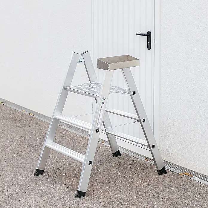 Munk Stehleiter Klapptritt beidseitig begehbar Alu natur 3 Stufen 2,73m AH - Anzahl Tritte: 3 Stk., Arbeitshöhe: 2.730 m, Aluminium - Silberne Aluminium-Stehleiter mit Ablageschale, im Freien vor einer weißen Wand und Tür stehend.