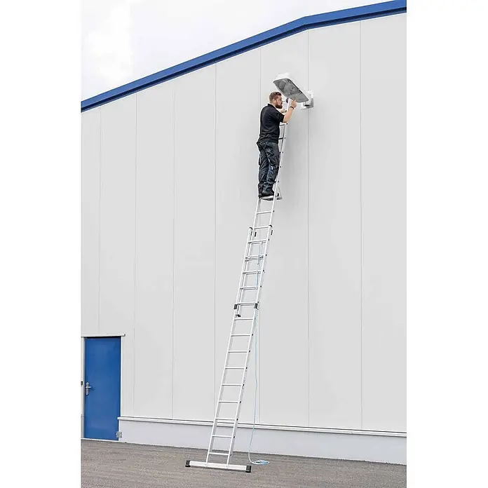 Munk Seilzugleiter Seilzugleiter mit Traverse 2x20 Sprossen - Anzahl Tritte: 20 Stk., Arbeitshöhe: 11.400 m, Aluminium - Silberne Anlegeleiter, an der eine Person eine Wandleuchte montiert.