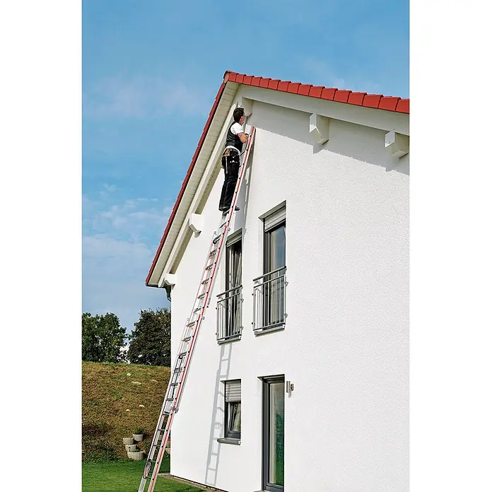 Hymer Seilzugleiter Seilzugleiter mit Wandlaufrollen 3x14 Sprossen - Arbeitshöhe: 9.840 m, Aluminium - Mann steigt auf silberner Anlegeleiter mit roten Akzenten an weißem Haus, um Dach zu erreichen.