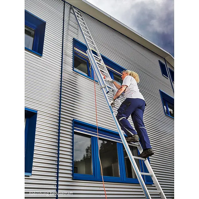 Mauderer Seilzugleiter Bavaria Seilzugleiter 960 mit gebogener Traverse 2x14 Dreikantsprossen - Anzahl Tritte: 14 Stk., Arbeitshöhe: 8.000 m, Belastbarkeit: 150 kg, Aluminium - Frau klettert eine hohe Aluminium-Ausziehleiter mit blauen Akzenten an einem silbernen Wellblechgebäude hoch.