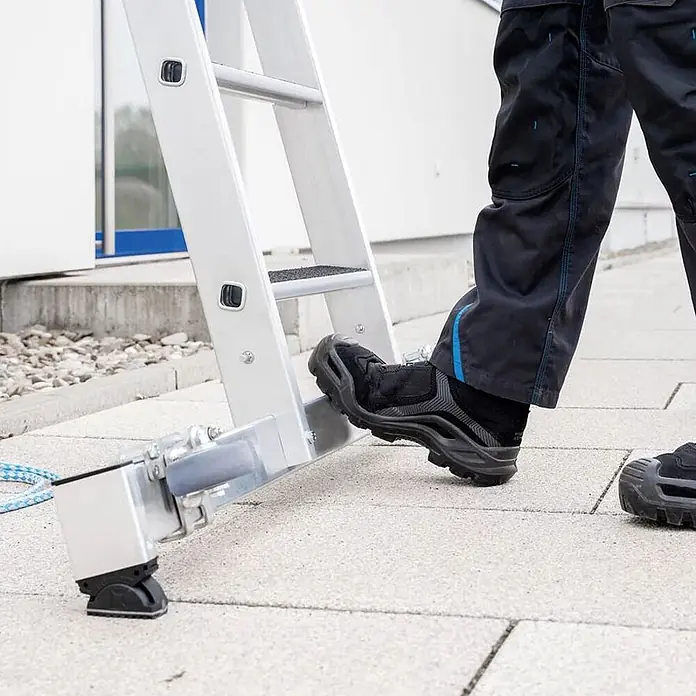 Munk Seilzugleiter Stufen- Seilzugleiter mit Nivello-Traverse und clip-step R13 2x12 Stufen - Anzahl Tritte: 12 Stk., Arbeitshöhe: 7.000 m, Aluminium - Person betritt Aluminiumleiter mit verstellbarem, rutschfestem Nivellierfuß auf gepflastertem Untergrund.