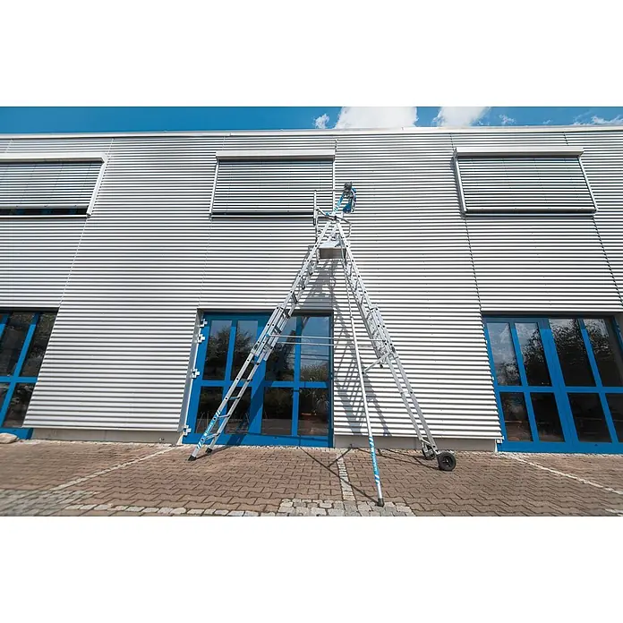 Zarges Teleskopleiter Teleskop Plattformleiter ZAP Masterflex Plus S gebördelt 3-5 Stufen - Anzahl Tritte: 5 Stk., Arbeitshöhe: 3.280 m, Belastbarkeit: 150 kg, Aluminium - Silberne Aluminium-Mehrzweckleiter an Wellblechfassade, reicht bis zum Fenster über blauen Türen.