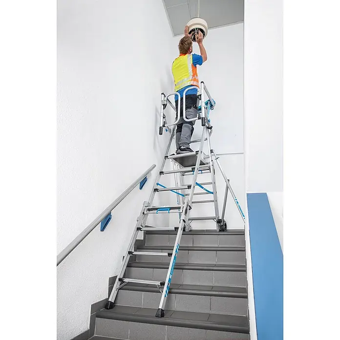 Zarges Teleskopleiter Teleskop Plattformleiter ZAP Masterflex Plus S gebördelt 3-5 Stufen - Anzahl Tritte: 5 Stk., Arbeitshöhe: 3.280 m, Belastbarkeit: 150 kg, Aluminium - Silber-blaue Mehrzweck-Treppenarbeitsplattform, von einem Arbeiter auf einer Treppe zur Montage einer Deckenleuchte genutzt.