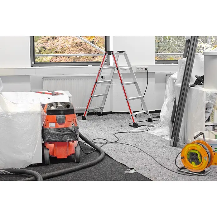 Hymer Stehleiter Stufenstehleiter eloxiert 2x4 Stufen - Anzahl Tritte: 4 Stk., Arbeitshöhe: 2.420 m, Aluminium - Renovierungsszene mit silberner und roter Stehleiter, orangem Industriestaubsauger und gelber Kabeltrommel in einem Raum.