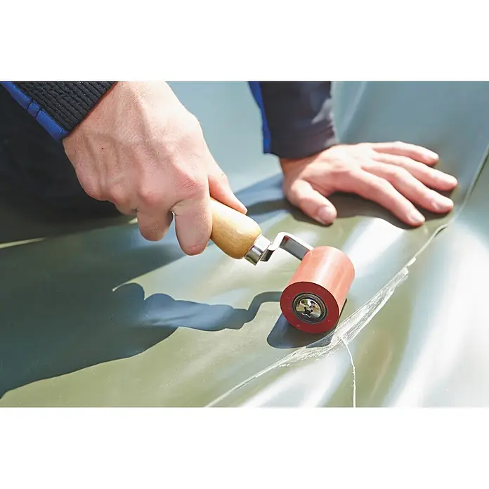 Oase PVC-Folienkleber - 1.000 ml - Person verwendet einen Handroller mit Holzgriff und roter Walze, um eine Naht auf grünem Material zu glätten.