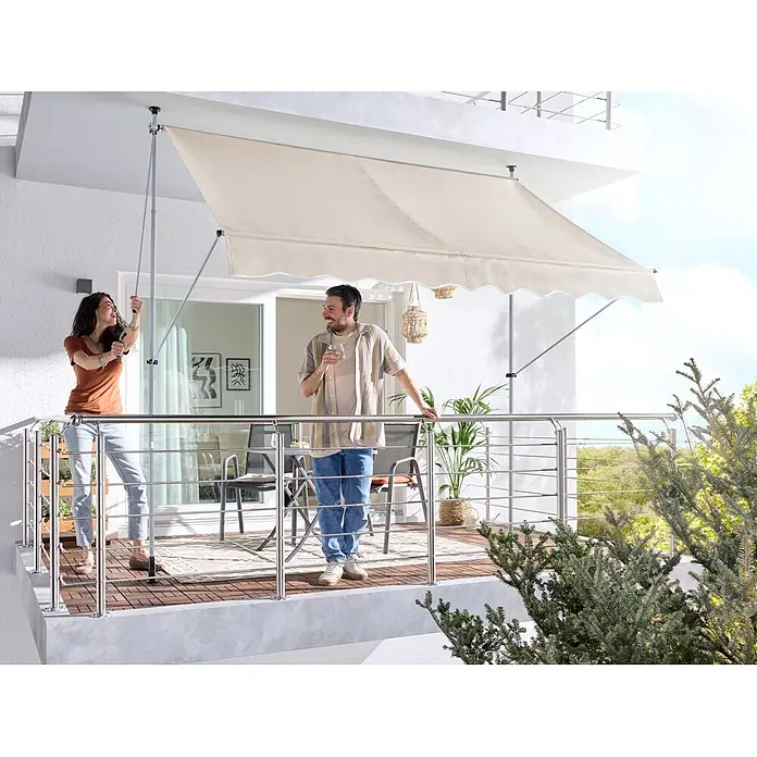 Sunfun Klemmmarkise - Beige, Breite: 3 m, Ausfall: 1,3 m - Cremefarbene manuelle Balkonmarkise auf einem Balkon ausgefahren. Eine Frau bedient sie mit einer Kurbel.
