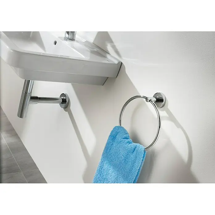 Roca Twin Toallero de anilla - Pegado - Una toalla azul cuelga de un toallero de aro plateado junto a un lavabo blanco en la pared. Práctico accesorio de baño.