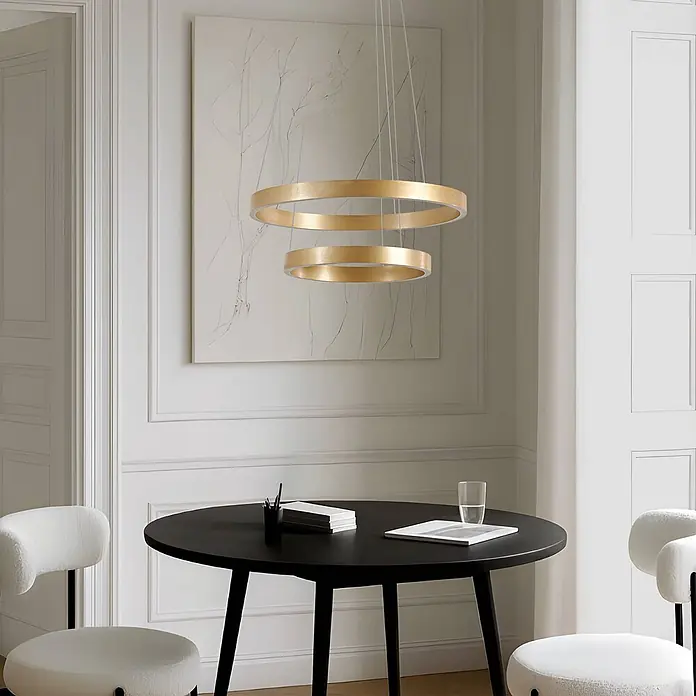 Lucande Pendelleuchte Yonam - L x B x H: 60 x 60 x 4,5 cm, messing / gold, gold, weiß - Goldfarbene Doppelring-Pendelleuchte über einem schwarzen runden Tisch mit Stühlen in einem modernen Raum.