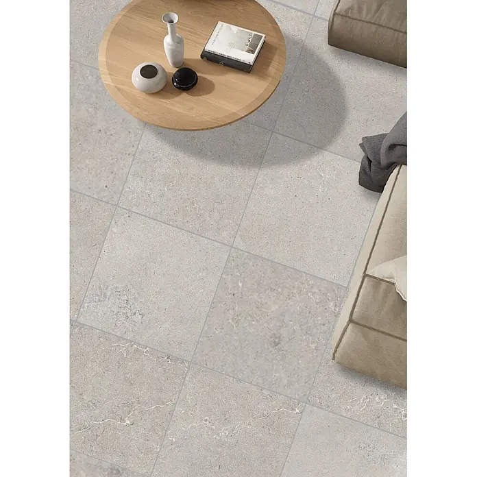 RAK Ceramics Feinsteinzeugfliese Valdi - 120 x 120 cm, Light Grey, Matt - Helle, großformatige, texturierte Bodenfliesen in Grau mit feinen Äderungen und Fugen, verlegt in einem Wohnzimmer.